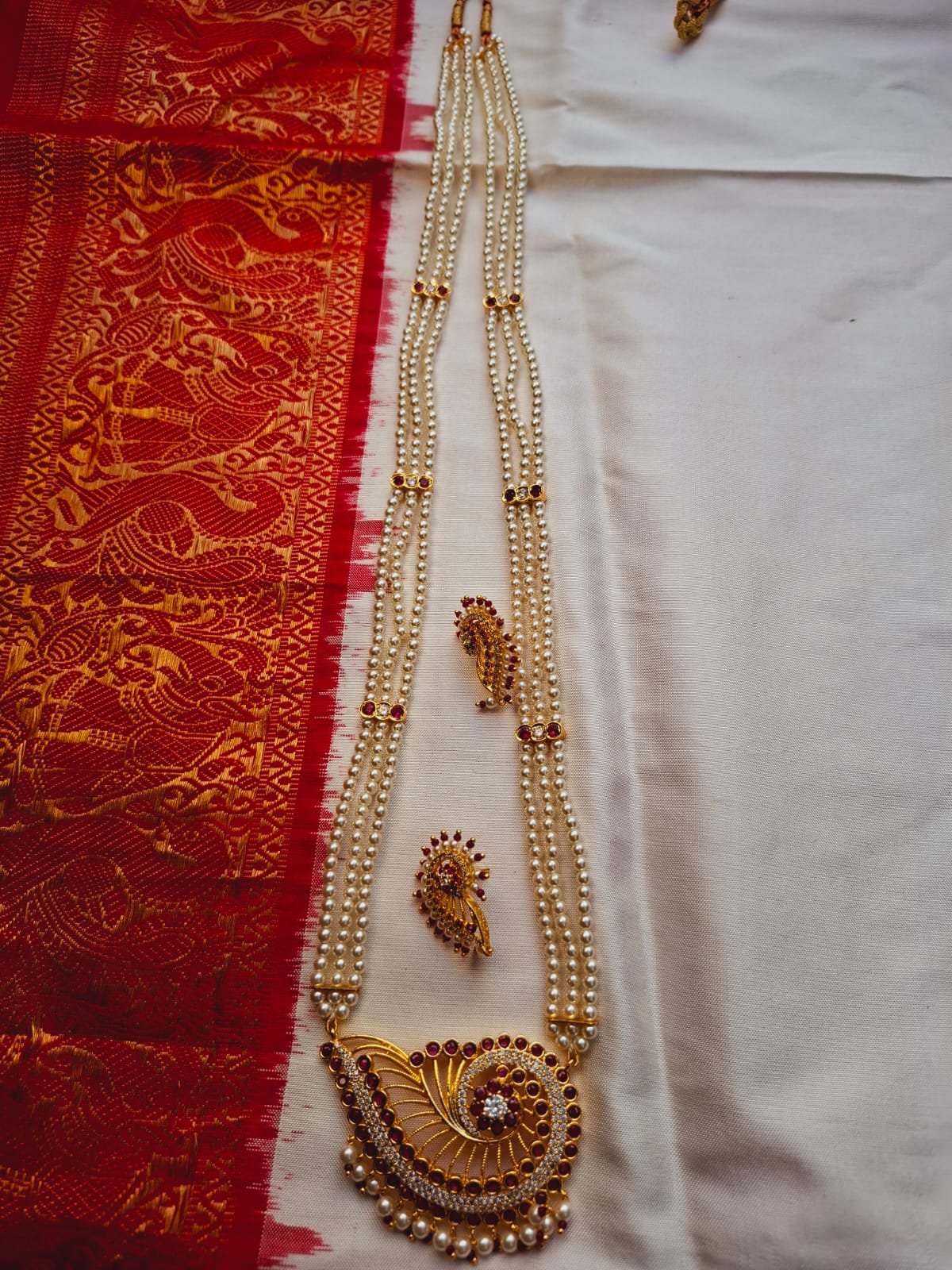 Ornate gold-toned necklace with intricate pendant on red and white ethnic textile backdrop