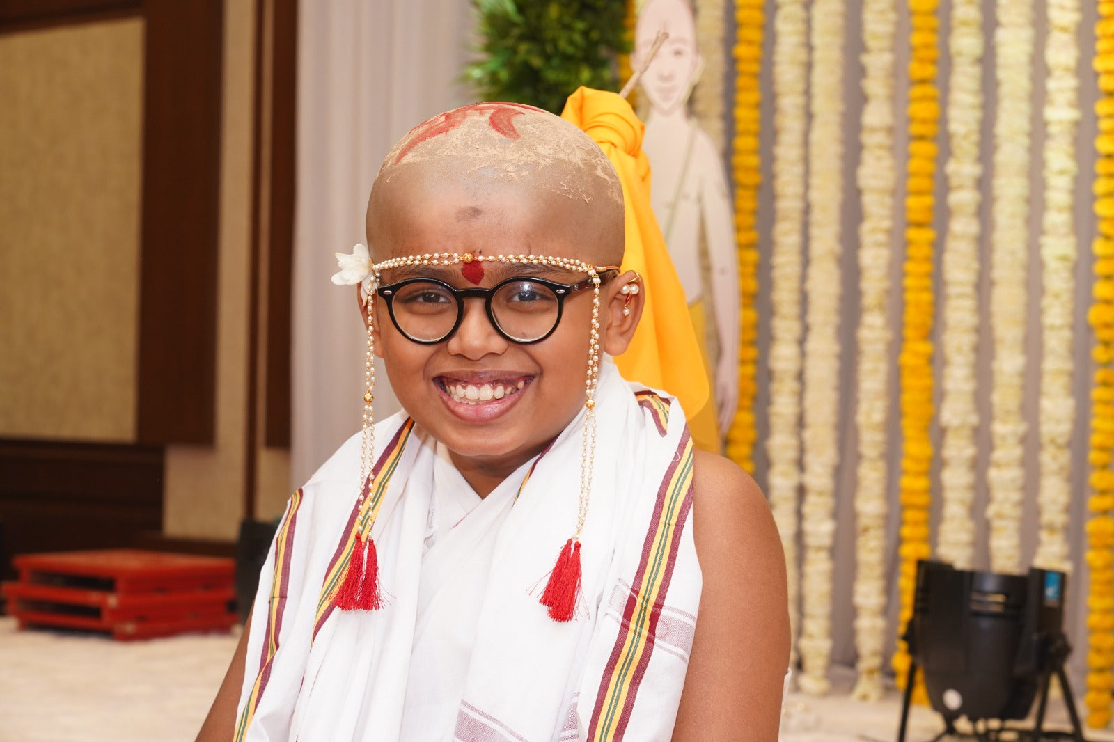 Colorful traditional headpiece, smiling woman with glasses, cultural decorations in the background