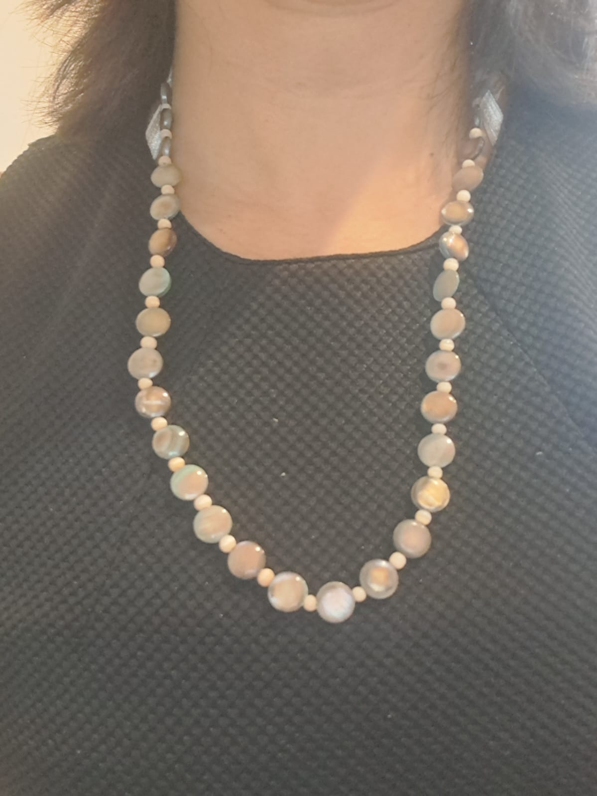 Elegant necklace made of natural seashells showcased on a black-patterned fabric, highlighting the unique textures and organic beauty of the shells.