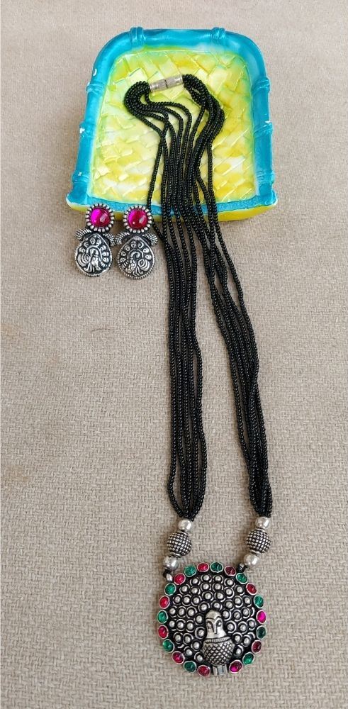 Vibrant oxidized short mangalsutra with intricate floral pendant and earrings set against a colorful abstract background.