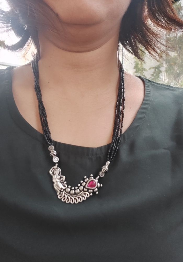 Elegant oxidised short mangalsutra with intricate floral motifs and a vibrant red stone, showcased against a black outfit.