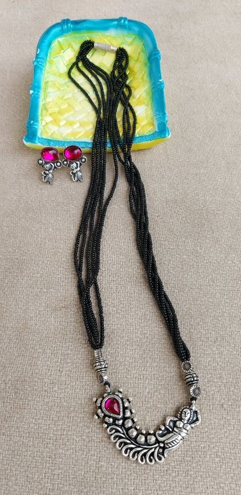 Oxidized short mangalsutra with intricate floral design and pendant, displayed on a colorful background.