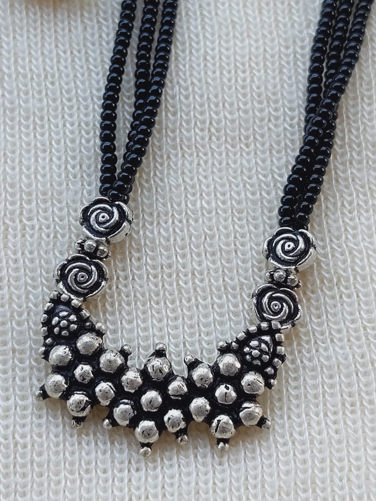 Elegant designer oxidized short mangalsutra with intricate spiral and floral motifs, showcased on a cozy knitted background.