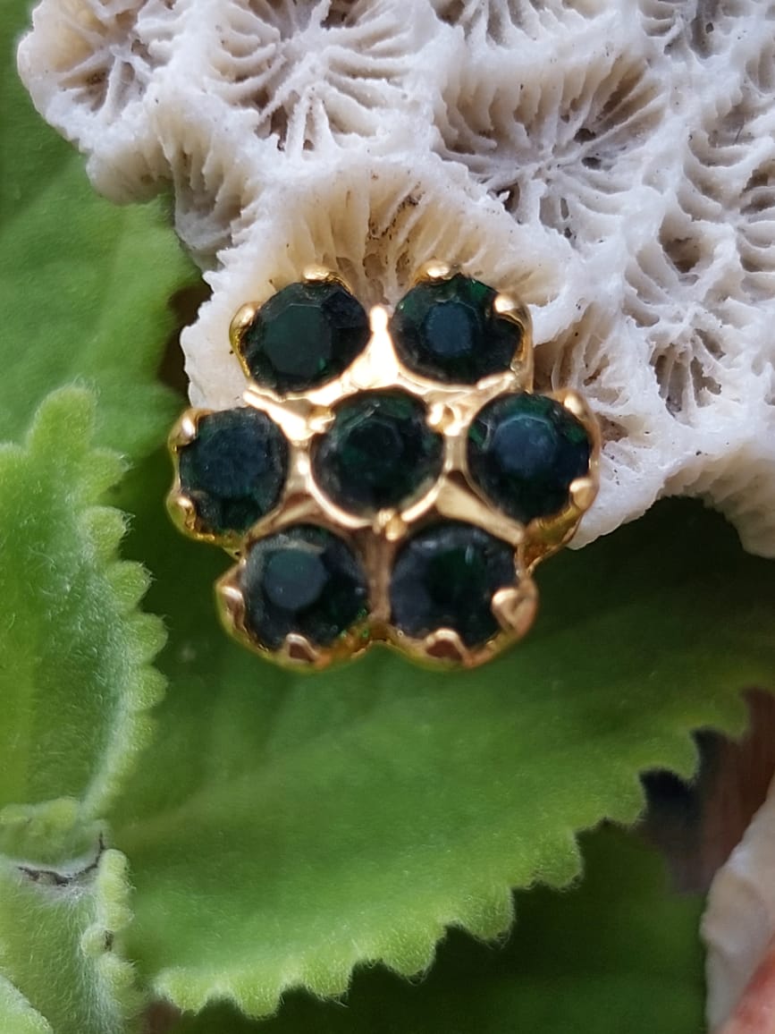 Elegant Green Stone Kudi - Intricate golden floral design with dark green gemstones set in the Mugdha Jewellery Store product, placed on a lush green leaf background.