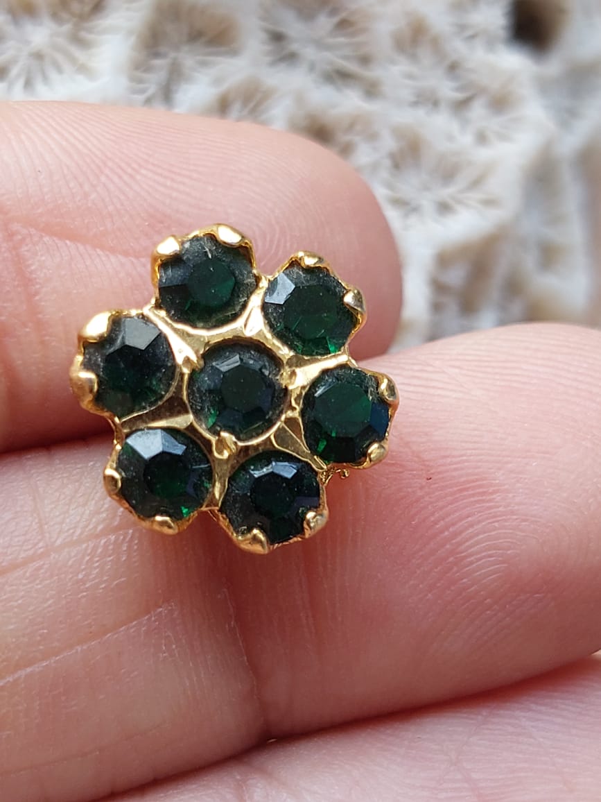 Elegant green stone kudi ring with a floral design, showcasing a cluster of deep green gemstones set in a gold-tone metal frame, held between fingers against a soft, blurred background.