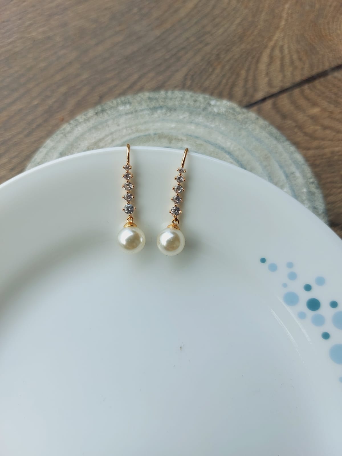 Elegant pearl and crystal drop earrings displayed on a white ceramic plate with a wooden background