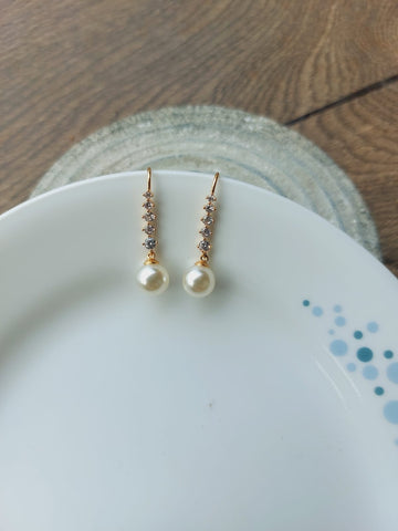 Elegant pearl and crystal drop earrings displayed on a white ceramic plate with a wooden background