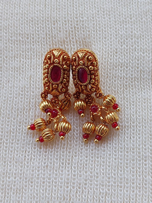 Antique golden earrings with intricate floral designs and sparkling red gemstones, displayed on a plain white knit fabric background.