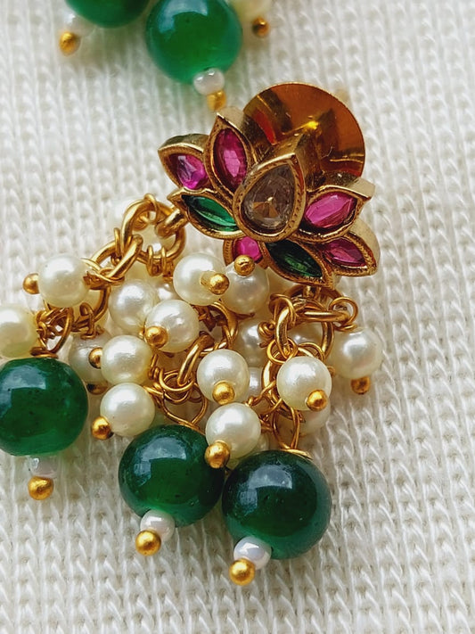 Ornate golden lotus necklace with vibrant green gemstones and lustrous white pearls, displayed on a soft knitted surface.