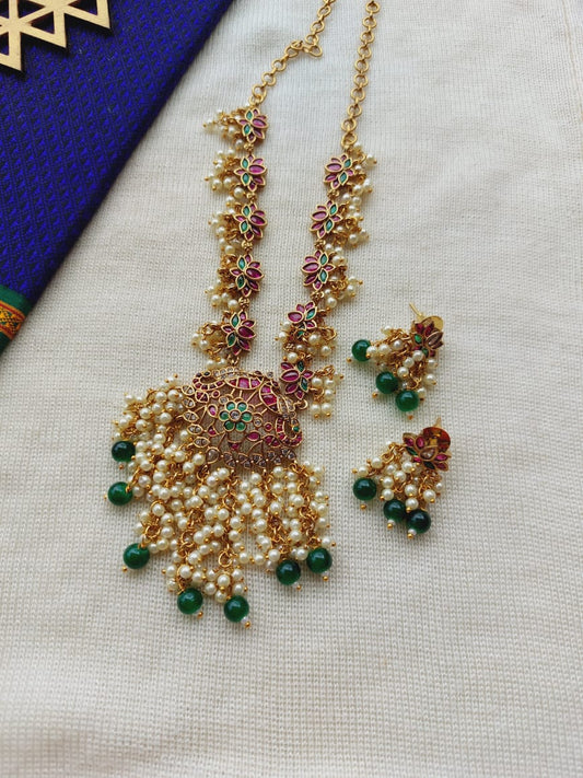 Exquisite Maharani Designer Lotus Necklace from Mugdha Jewellery Store showcases intricate golden floral patterns, lustrous pearls, and vibrant gemstones.