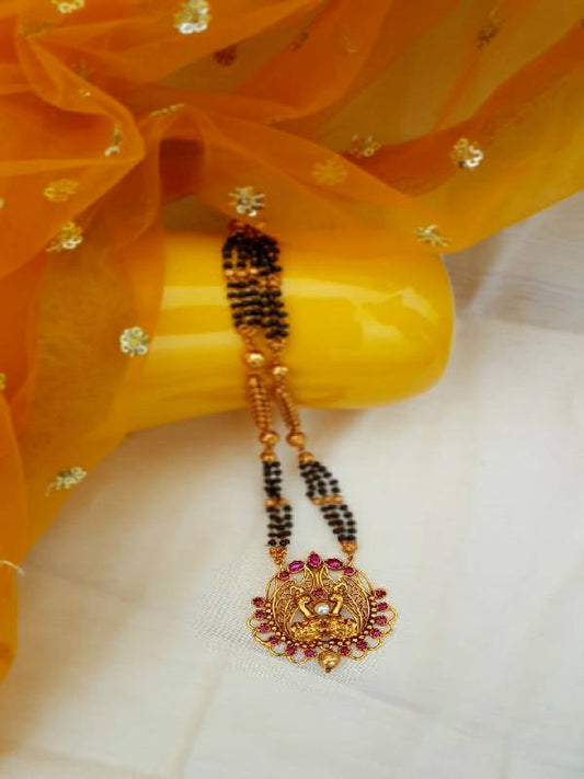 Antique designer mangalsutra with intricate floral pendant and beaded chain, showcased against a vibrant orange flower backdrop.