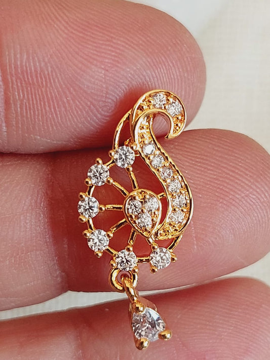 Decorative gold-colored pendant with intricate floral and scroll design, adorned with sparkling diamonds or crystal stones, held between fingers.