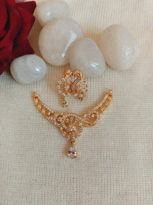 Elegant gold-toned American diamond brooch with floral and bird design, nestled among white stones on a knitted background.