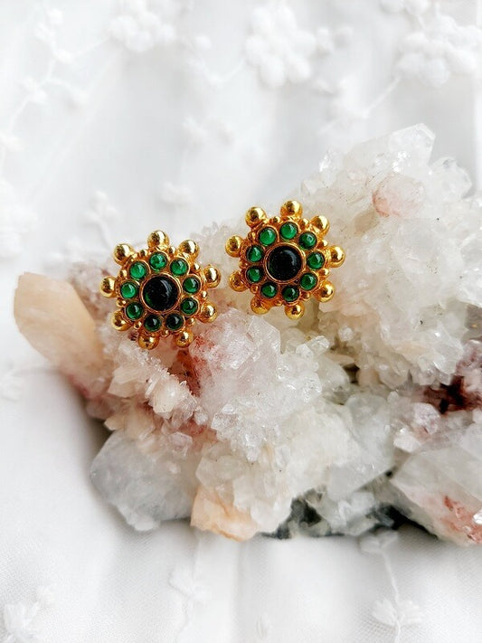 Elegant gold-tone earrings with vibrant green and black gemstones, resting on a bed of sparkling quartz crystals