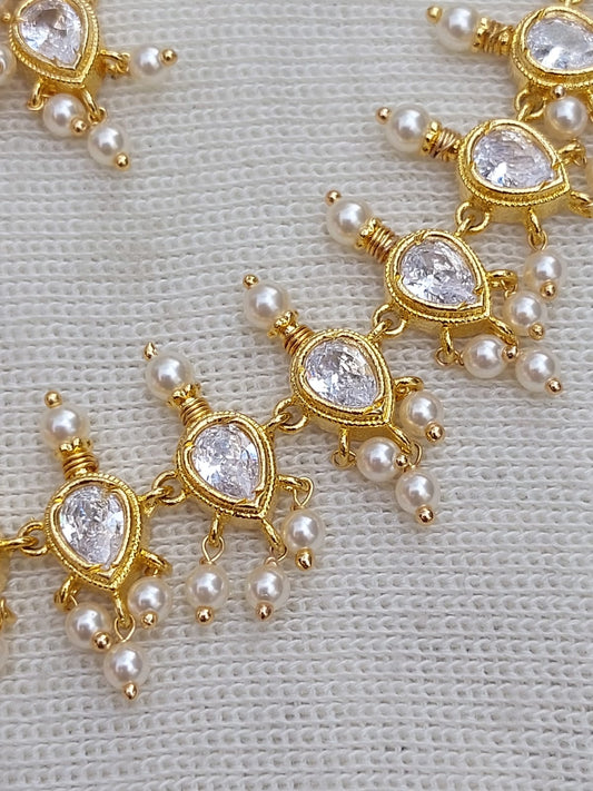 Elegant gold-toned necklace adorned with sparkling teardrop-shaped crystals and delicate pearls, showcased on a light-colored background.