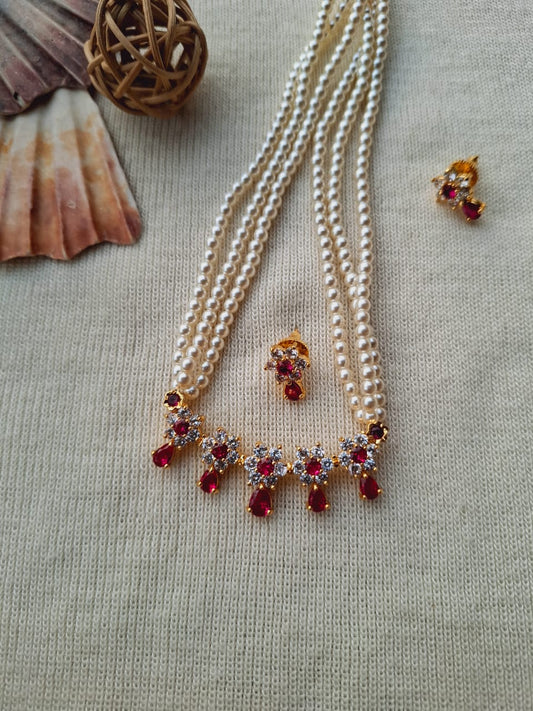 Elegant pearl necklace with vibrant red gemstone accents, displayed on a neutral fabric background alongside other jewelry pieces.