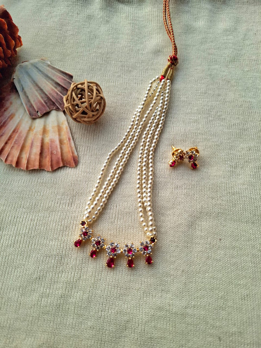 Elegant gold necklace with vibrant red and purple gemstones, complemented by a decorative metal pendant and seashell ornaments, showcased on a light-colored fabric background.