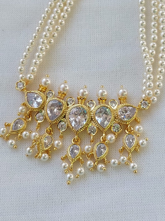 A necklace with intricate gold-toned pendants and sparkling crystal accents, complemented by multiple strands of shimmering white pearls, decorating a neutral-toned fabric background.