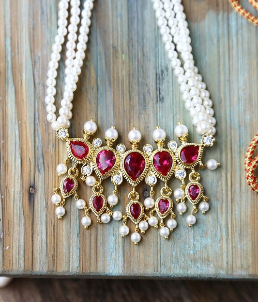 Elegant traditional Indian Puneri Tanmani necklace with multiple strands of pearls and a golden pendant featuring vibrant red gemstones and intricate floral design. The necklace is placed on a rustic wooden surface.