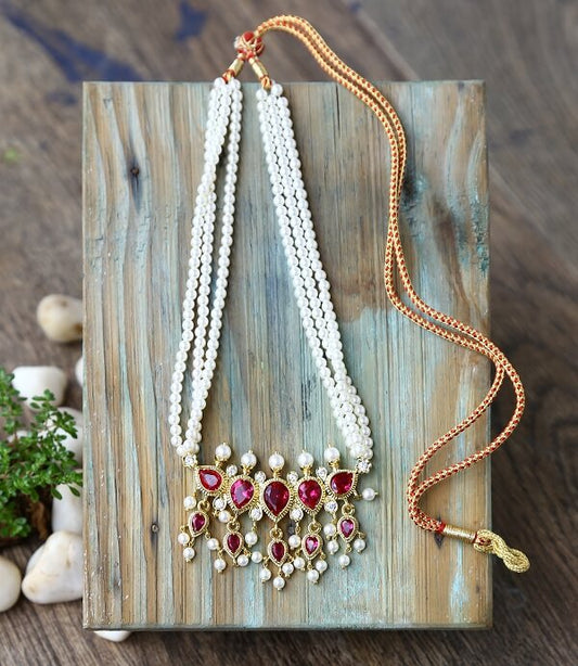 Elegant pearl and gold necklace with ornate ruby-accented pendant on a wooden display stand.