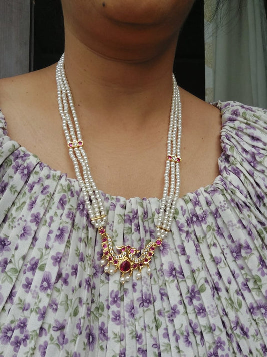 Designer Two Peacock Short Haar, elegant pearl necklace with vibrant gemstone pendant, gracefully displayed against a floral patterned dress.