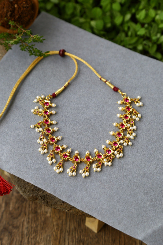 Beautiful Gold and Red Traditional Designer Necklace on Gray Background with Lush Greenery