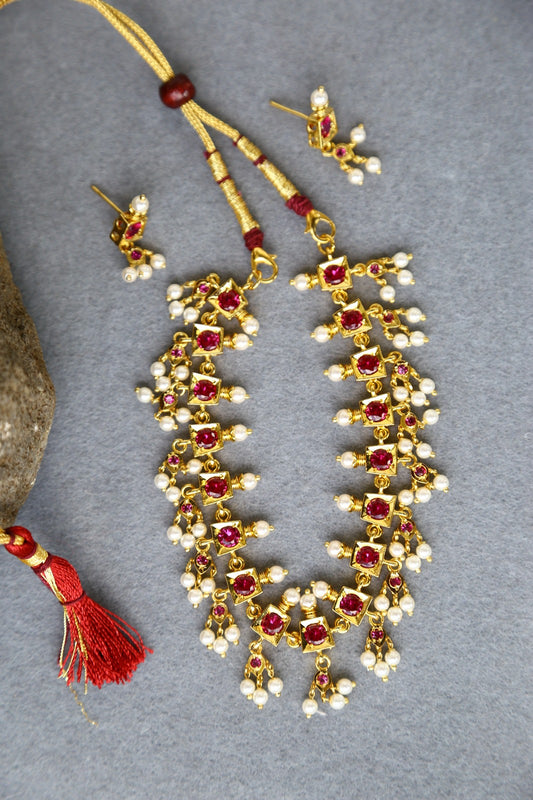 Elegant red and gold traditional designer jewelry set from Mugdha Jewellery Store, featuring a necklace with intricate pearl and ruby embellishments.