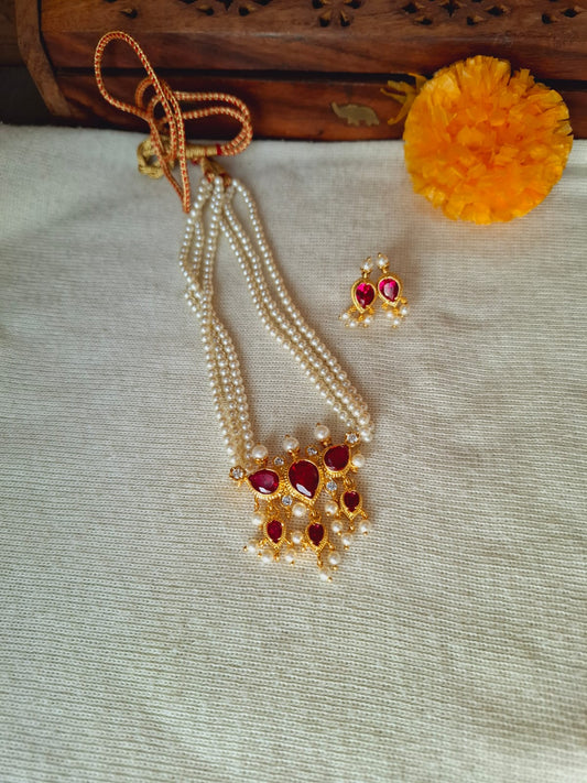 Ornate traditional Puneri 3-stone tanmani necklace with pearl strands and ruby accents, displayed on a fabric surface alongside a marigold flower.