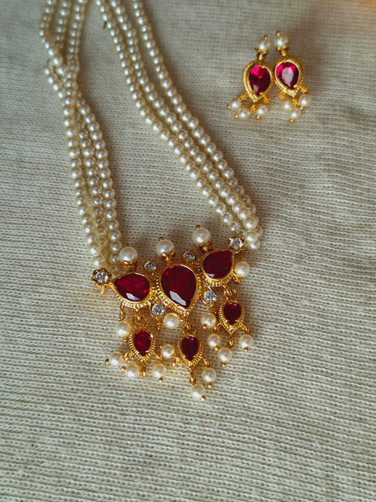 Elegant pearl necklace and earrings set with ruby-colored gemstones, featuring a pendant design and delicate gold-toned accents from the Mugdha Jewellery Store.